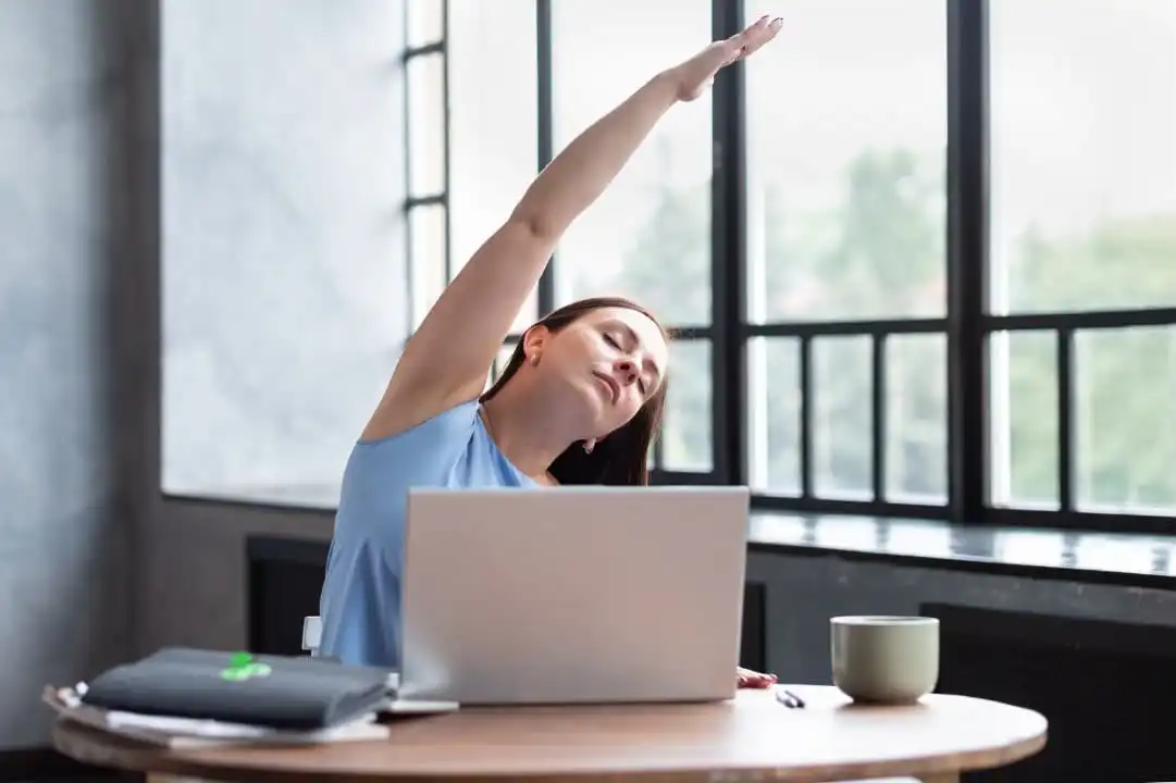 A woman stretching her arm in front of her laptop for an employee wellness program