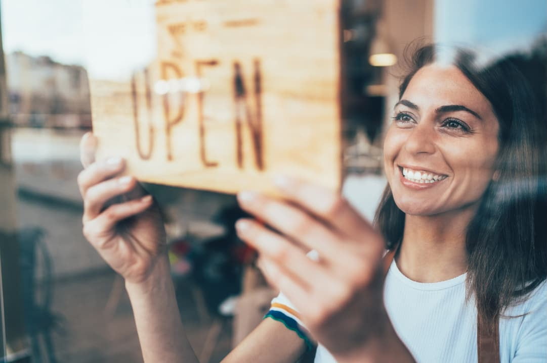 A woman putting up an “Open” signage in front of her start up business