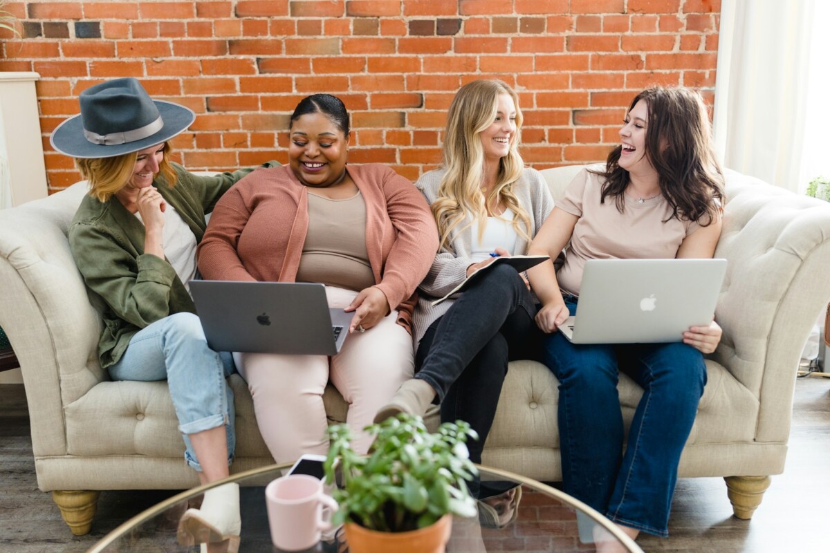 group of women sitting on the couch and holding laptop