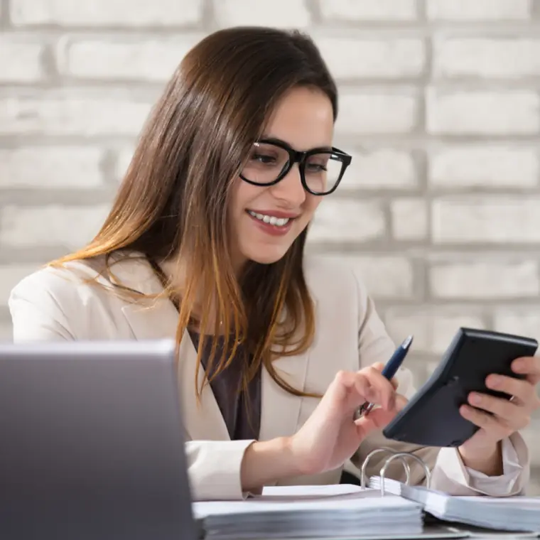 Smiling HR professional with glasses checking payroll figures at her desk